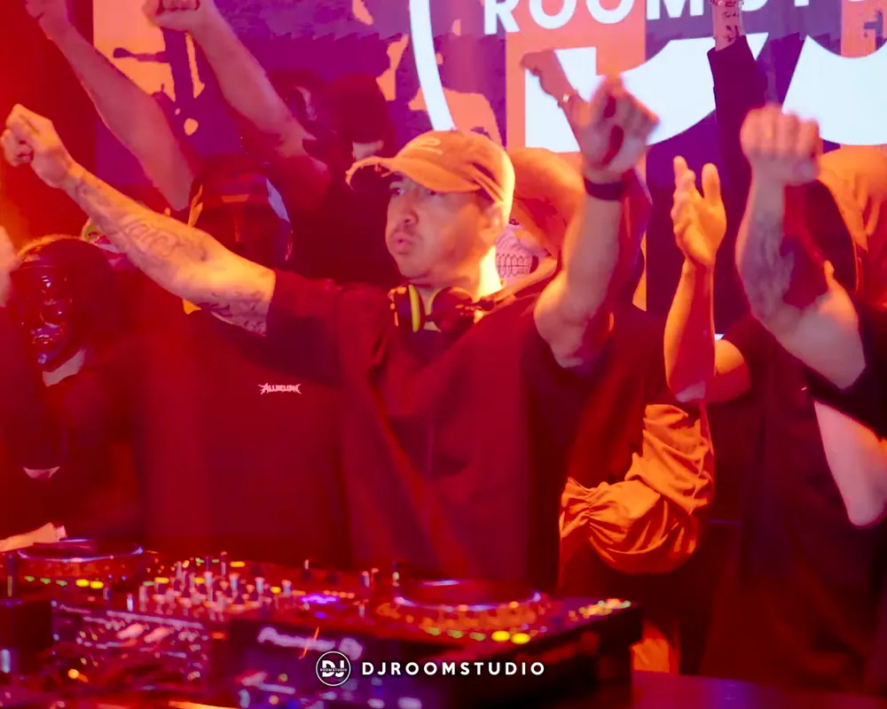 DJ met een crowd in maskers die de handen in de lucht steekt in DJ Room Studio